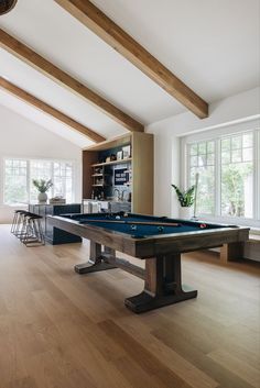 a pool table in the middle of a living room with wood floors and exposed beams