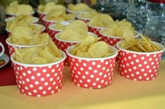 red and white polka dot cups filled with potato chips on a yellow tablecloth covered table