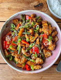 a bowl filled with chicken and veggies next to rice on a wooden table