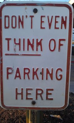 a red and white sign that says don't even think of parking here on it