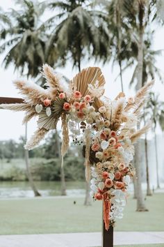 an arrangement of flowers and feathers is displayed on a wooden pole in front of palm trees