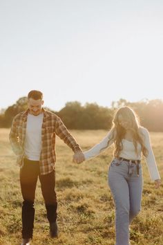 a man and woman holding hands while walking through an open field