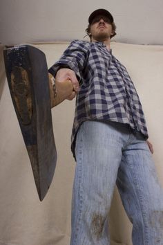 a man holding a large wooden object in his right hand while standing against a wall