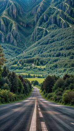 an empty road with mountains in the background and trees on both sides, surrounded by greenery