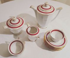 a white table topped with lots of red and white dishes covered in saucers, cups and saucers