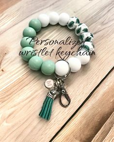 the personalized bracelet with green and white beads is shown on a wooden table next to a keychain