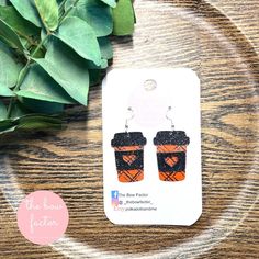 an orange and black cup shaped earrings sitting on top of a wooden table next to green leaves