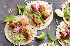 three tacos with meat, onions and cilantro on a black surface next to lime wedges