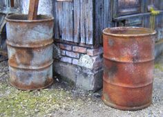 two rusty barrels sitting next to each other on the ground near a building with an old door