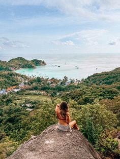 a woman sitting on top of a rock looking out at the ocean and land below