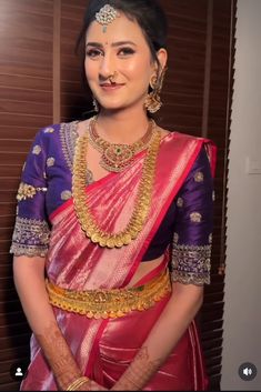 a woman in a pink and purple sari with gold jewelry on her neck, smiling at the camera