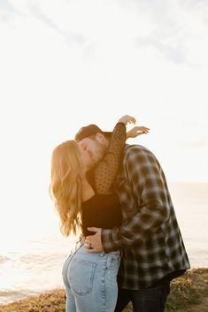 a man and woman kissing on the beach with the ocean in the background at sunset