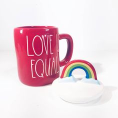 a red coffee mug with love is equal written on it next to a rainbow cookie