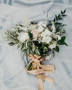 a bouquet of white flowers and greenery tied to a ribbon on a bed sheet