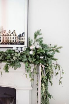 a white fireplace mantel with greenery and ornaments in front of the fire place