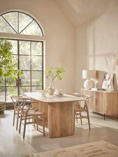 a dining room table with chairs and a potted plant in the center surrounded by windows