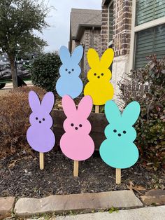 four wooden easter bunnies with faces painted on them in front of a brick house