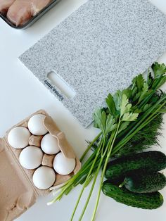 an assortment of vegetables and eggs laid out on a white surface next to a cutting board