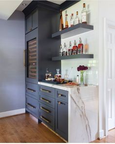 a kitchen with blue cabinets and marble counter tops, along with shelves filled with liquor bottles