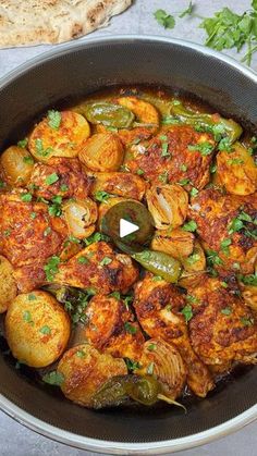 a pan filled with chicken and potatoes covered in green sauce next to pita bread