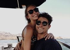 a man and woman on a boat in the ocean smiling at the camera with their arms around each other