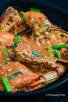 cooked crabs with green onions and carrots in a black bowl on a dark surface