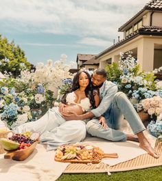 a pregnant couple sitting on the ground in front of flowers