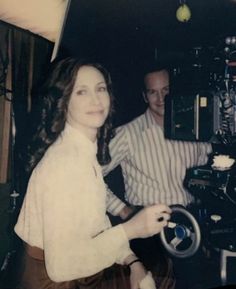 an old black and white photo of a woman holding a steering wheel with a man in the background