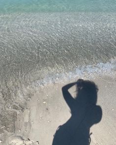 a shadow of a person standing on the beach with their hand in her hair and looking down at the water