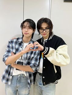 two young men standing next to each other in front of a white wall and wearing glasses