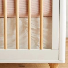 a white crib with wooden slats and pink sheets