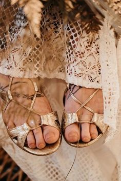 a woman wearing gold sandals standing on top of a white lace covered floor next to a plant