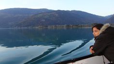 a woman standing on the edge of a boat looking out over water with mountains in the background