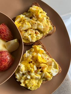 two pieces of toast with scrambled eggs and an apple