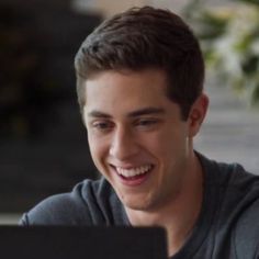 a young man smiles while looking at his laptop