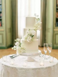 a white wedding cake sitting on top of a table next to wine glasses and candles