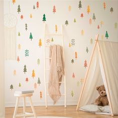 a teddy bear sitting in front of a teepee tent with trees on the wall