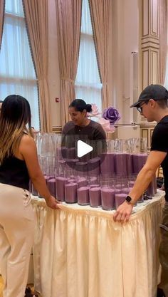 two people standing at a table with purple cups on it