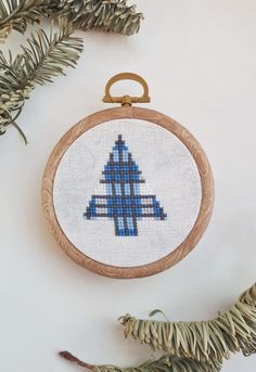 a cross stitch christmas ornament hanging from a tree branch with pine needles on it