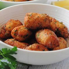 two bowls filled with fried food on top of a wooden table next to lemon wedges and parsley