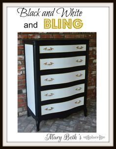 a black and white dresser with gold trimmings on the bottom, in front of a brick wall