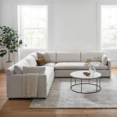 a living room with white walls and wood flooring, a large sectional couch in front of a round coffee table