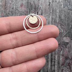 This pendant necklace is handmade from solid sterling silver, 14k yellow goldfill, and 14k rose goldfill. I have cut a small gold circle from a sheet of 14k yellow gold filled metal. I then soldered rings from 14k rose goldfill and sterling silver. I have hammered and finished each of the circles by hand. The pendant hangs from a sterling silver chain.Be sure to see all photos and video for size and finish reference.Outer Circle Size: Just over 3/4" acrossThe necklace features a lobster claw clasp and a 3-inch extender allowing it to be slightly adjustable. Select your desired length and chain finish when ordering. Note that the total length is measured from end-to-end and includes all parts of chain and clasp.The necklace photographed is shown at an 18-inch length modeled on a women's siz Soldered Rings, Circle Pendant Necklace, Gold Circle, Hammered Gold, Hammered Silver, Brass Pendant, Circle Pendant, Sterling Silver Necklace, Lobster Claw