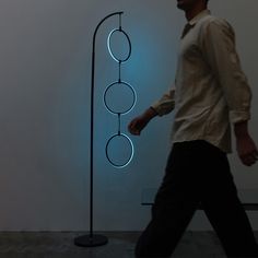 a man walking past a sculpture with circles on it's side and a blue light behind him