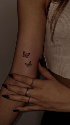 two hands holding each other with butterfly tattoos on their fingers and wristbands,