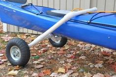 a blue kayak sitting on top of leaves in front of a building with a wheelbarrow attached to it