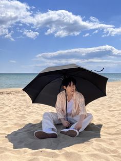 a man sitting on the beach under an umbrella with his feet propped up in the sand