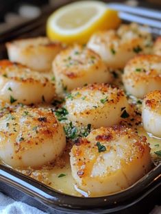 some sea scallops are in a pan with lemon wedges on the side