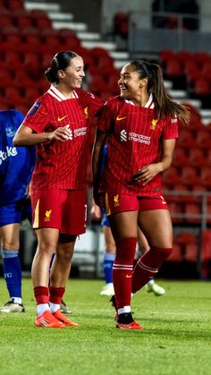 two women in red uniforms standing on a soccer field with their arms around each other