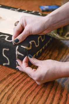 two hands are working on a piece of fabric that is sitting on a wooden table